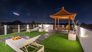 En tagterrasse med en traditionel sommerpavillon, liggestole og et lille bord med en potteplante.