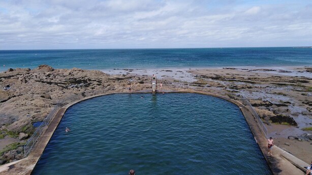 Une plage rocheuse avec une piscine entourée d’une rambarde en métal.