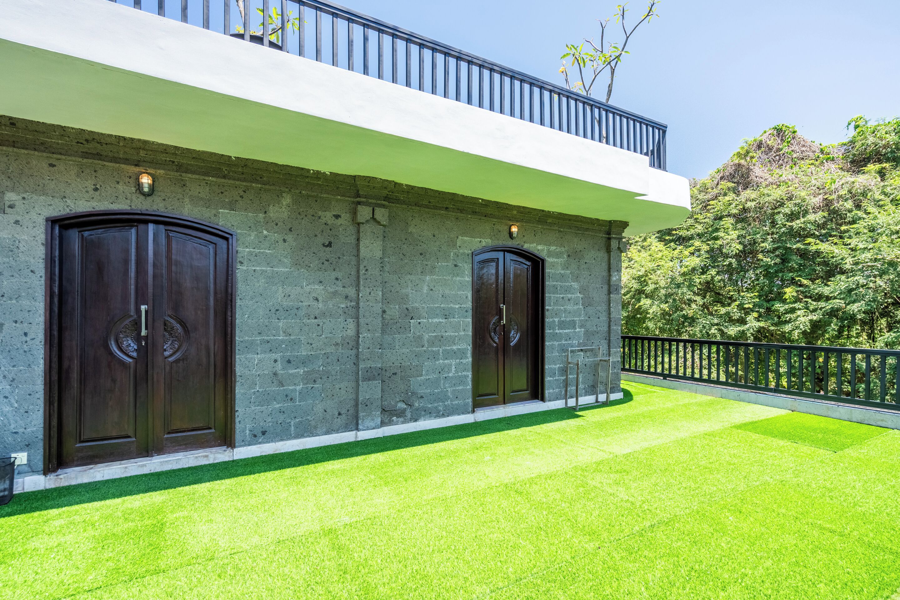 A modern building with two large wooden doors, a balcony, and a well-maintained lawn.