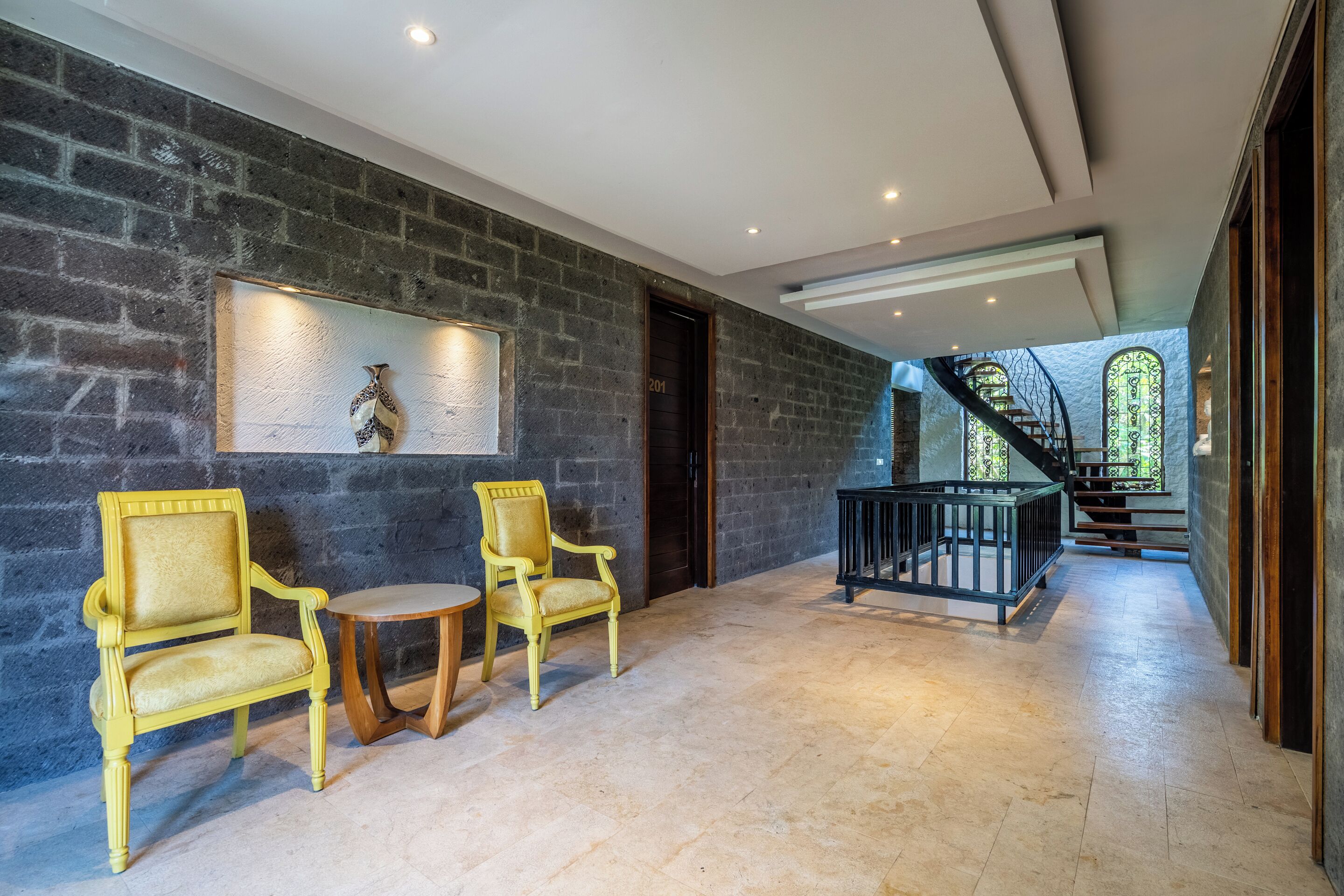 A spacious hallway with a stone wall, a staircase, and a view of greenery outside.