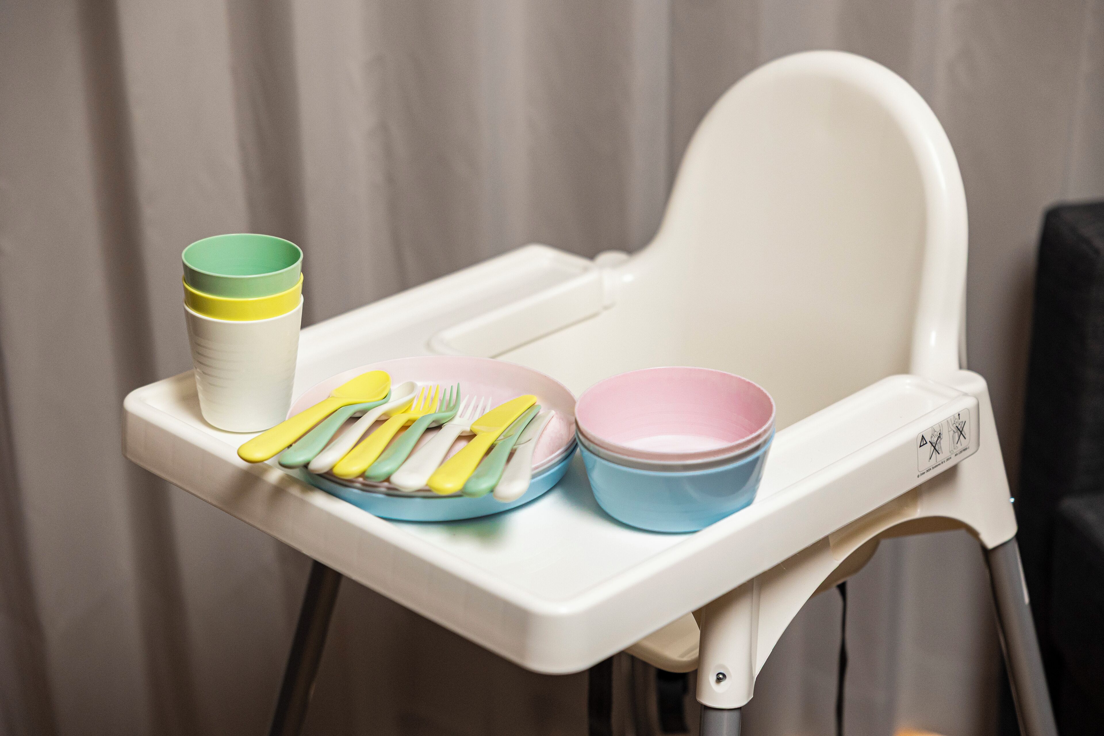 A high chair with a tray table holding a stack of cups, a bowl, and a plate with utensils.