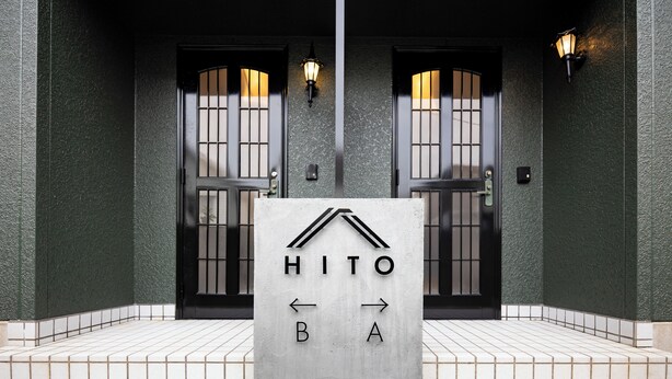 A building entrance with two doors, a sign with arrows pointing left and right, and a light fixture above each door. - HITO (Fukuoka)