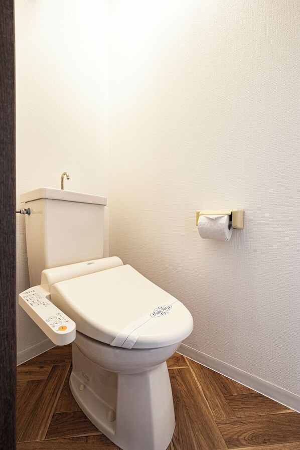 A modern toilet with a control panel, a toilet paper holder on the wall, and wooden flooring.