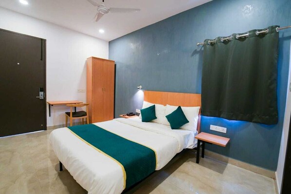 A hotel room with a bed, a desk, a chair, a nightstand, and a curtain.