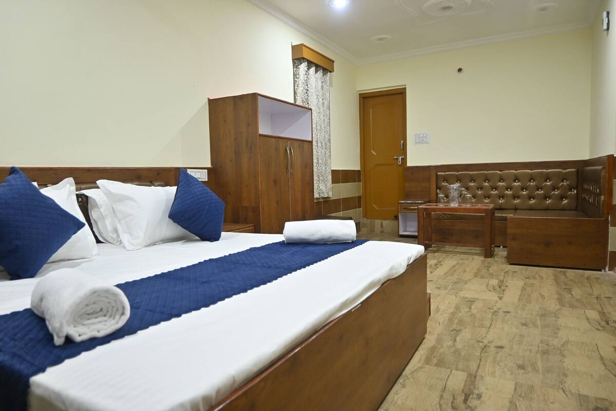 A hotel room with a large bed, wooden wardrobe, a seating area with a sofa and armchairs, and a door with a curtain.