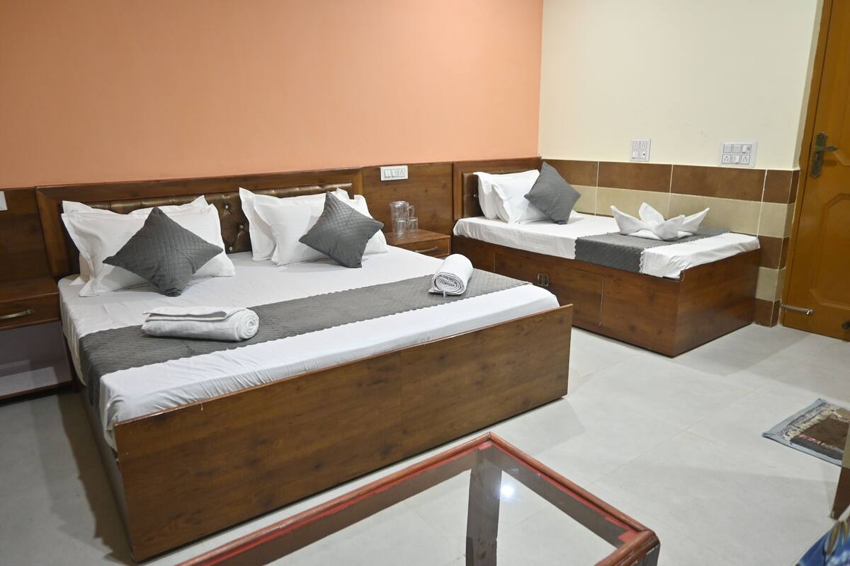 A hotel room with two beds, each with white linens and grey pillows, a wooden headboard, and a small bedside table with a glass top.