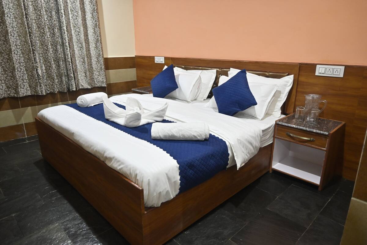A neatly made bed with white and blue bedding, a wooden headboard, and a nightstand with a glass pitcher.