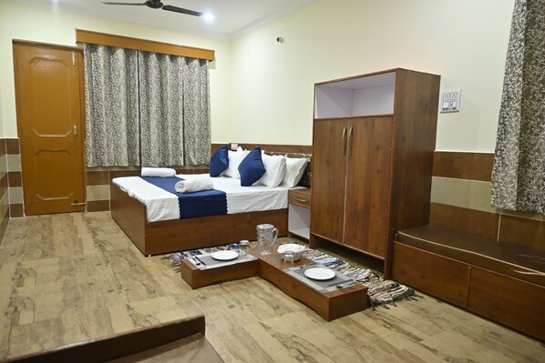 A hotel room with a bed, wardrobe, bedside table, and a small seating area.