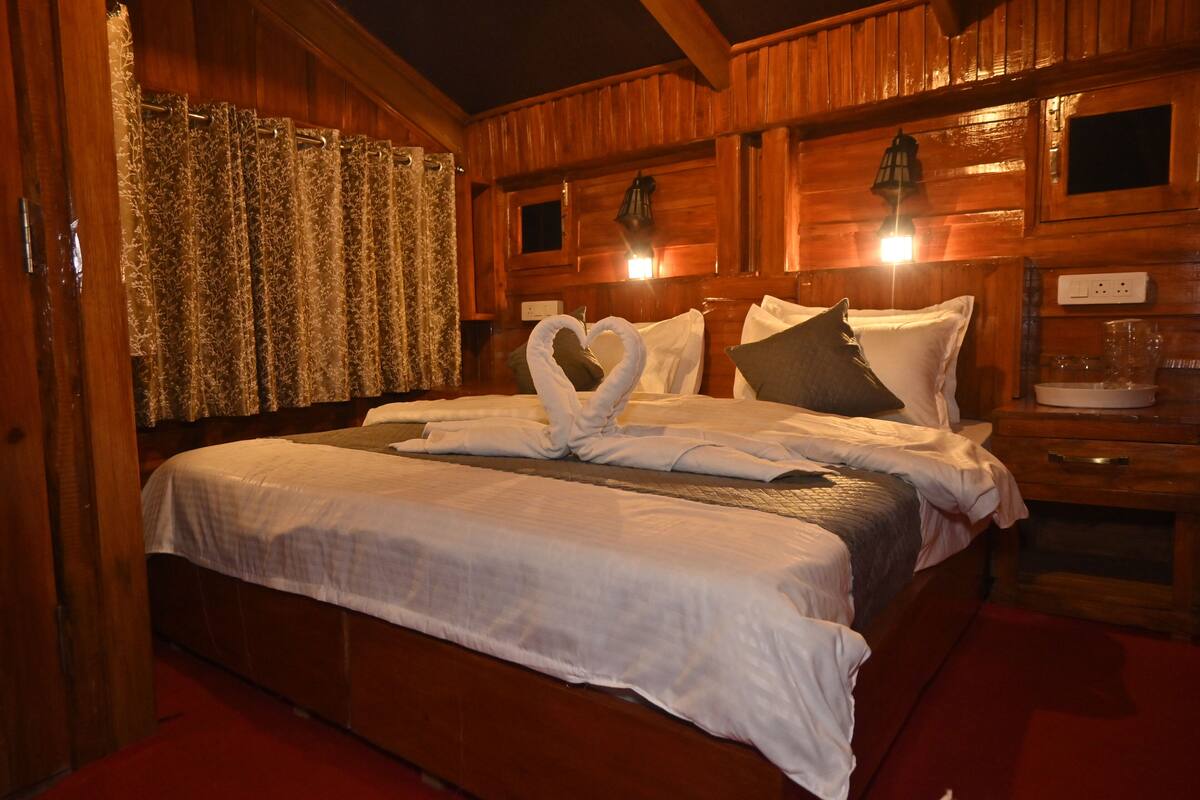 A wooden cabin-style bedroom with a large bed, a nightstand, and a wall-mounted lamp.