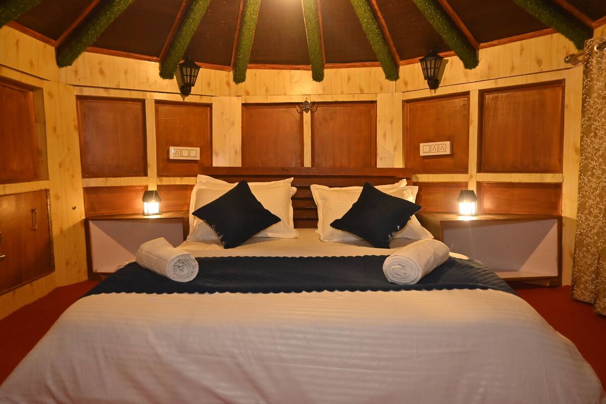 A double bed with white and black linens, two bedside tables with lamps, and wooden paneling on the walls.