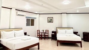 Habitación de hotel con dos camas, una mesita con sillas, una ventana y un equipo de aire acondicionado.