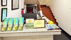 Una recepción de hotel con diplomas enmarcados, un reloj y un cartel que indica la zona de equipaje.