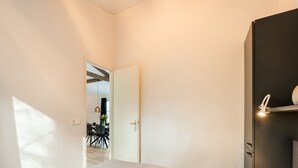 Quarto com cama, guarda-roupa e porta que dá para uma sala de jantar.