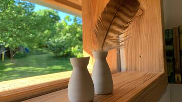 Dos jarrones blancos sobre una repisa de madera junto a una ventana con vistas a la vegetación.