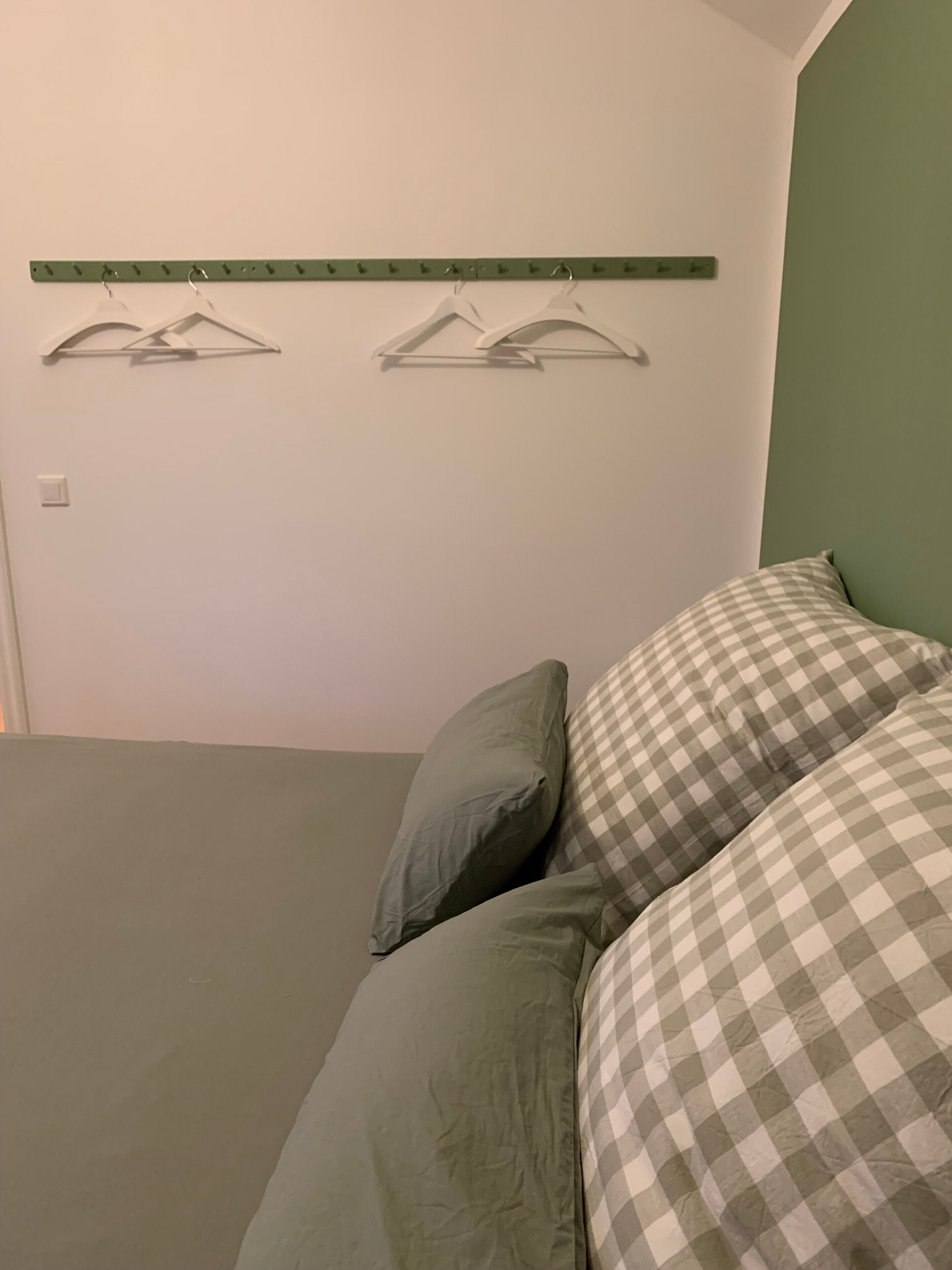 A bedroom with a bed, pillows, and a wall-mounted coat rack.