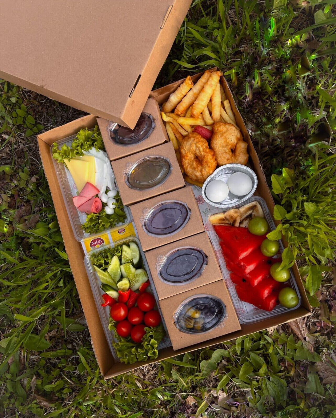 Una cesta de picnic con diferentes alimentos como sándwiches, papas fritas y frutas.