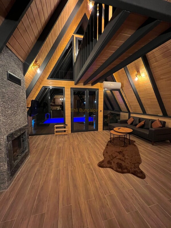 A spacious loft with high ceilings, exposed wooden beams, a fireplace, and a cozy seating area. - EHLI BUNGALOV (Sapanca)