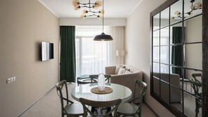 A dining area with a round table, chairs, a chandelier, a sofa, and a large mirror.
