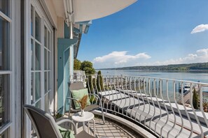 Un balcon donnant sur un lac, avec une balustrade blanche et une petite table sur laquelle est posé un vase.