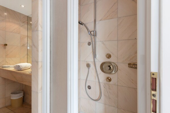 Une salle de bain avec une douche, un porte-serviettes et une poubelle.