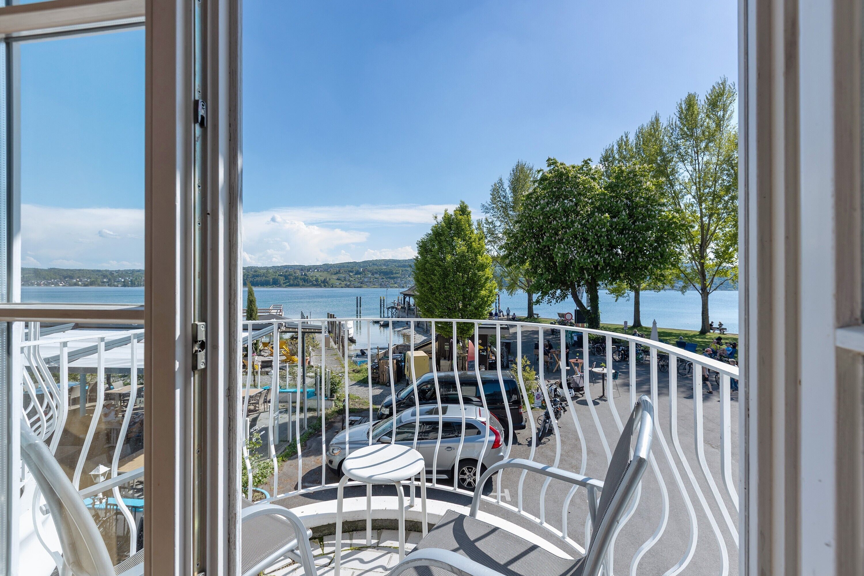 A balcony with a view of a lake, parked cars, and a tree.