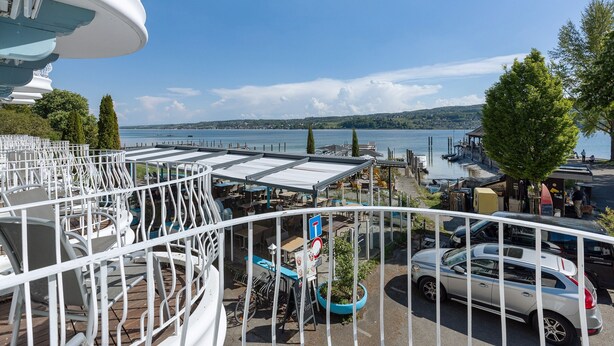 A seaside view with a dining area, a car, and a boat dock. - Room 'Mit Seeblick Und Balkon' with Lake View, Shared Terrace and Wi-Fi (Reichenau)