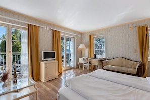 A hotel room with a bed, a desk, a television, a chair, and a balcony with curtains. - Room 'Mit Seeblick Und Balkon' with Lake View, Shared Terrace and Wi-Fi (Reichenau)