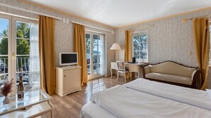 A hotel room with a bed, a desk, a television, a chair, and a balcony with curtains. - Room 'Mit Seeblick Und Balkon' with Lake View, Shared Terrace and Wi-Fi (Reichenau)