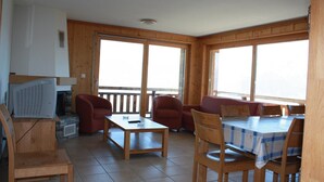 A room with a wooden interior, a fireplace, a television, and a dining area with a table and chairs. - Charming apartment with ski storage (Veysonnaz)