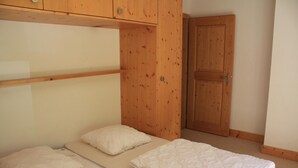 A small, single-bed room with a wooden wardrobe and a door. - Charming apartment with ski storage (Veysonnaz)