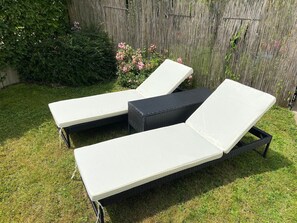 Deux fauteuils de jardin, dotés de coussins blancs, sont placés sur une pelouse verdoyante, avec une clôture en bois et de la végétation en arrière-plan.