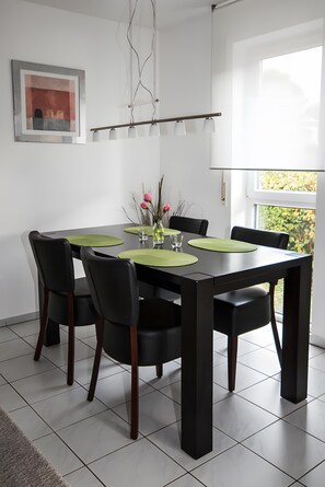 Et spiseområde med et sort bord, grønne servietter, sorte stole, en vase med blomster og et billede i ramme på væggen.