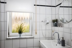 Et badeværelse med et vindue, en vask, et spejl og en telefon.