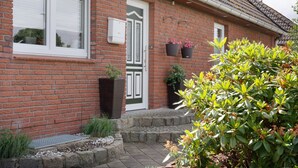 Una casa de ladrillo con una puerta blanca, una ventana con persianas y plantas en macetas.