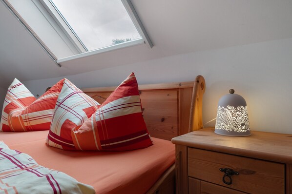 Ein Schlafzimmer mit Dachfenster, einem Bett mit gestreifter Bettwäsche, einem Nachttisch mit Lampe und einem Holznachtkästchen.