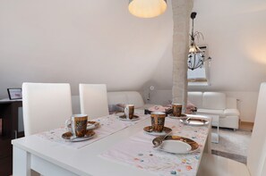 Un coin repas avec une table dressée pour quatre personnes, des chaises blanches, un lustre et un canapé blanc en arrière-plan.