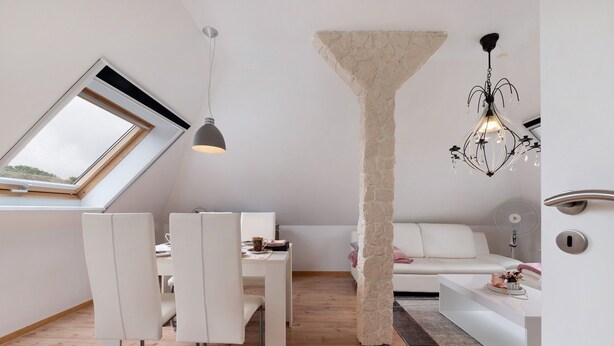 Un dormitorio estilo loft moderno con tragaluces, una columna de piedra, un sofá blanco y una zona de comedor con sillas blancas.