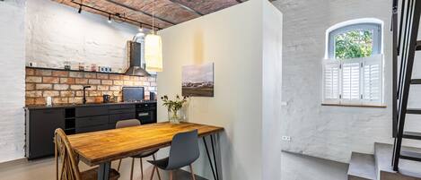A kitchen with a brick wall, a wooden dining table, and a window with shutters.