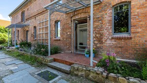 A brick building with a covered entrance, steps leading to the door, and a garden area with plants and flowers. - Apartment in Former Horse Stable (Angermünde)