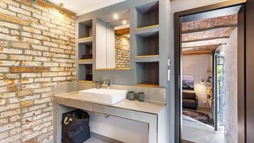 A modern bathroom with a large sink, a mirror, and a brick wall.