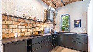 A kitchen with a brick wall, modern appliances, and a window with a view. - Apartment in Former Horse Stable (Angermünde)