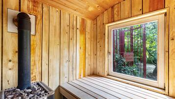 Ein Saunaraum mit Holzwänden, einer Sitzbank, einer Saunaheizung und einem Fenster mit Blick auf Bäume.