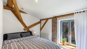 A bedroom with a sloped ceiling, a large bed, a window with curtains, and a brick wall. - Apartment in Former Horse Stable (Angermünde)