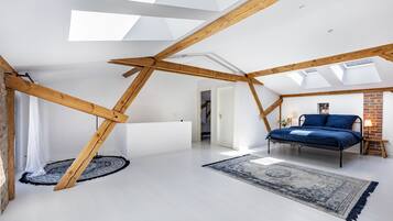 A loft bedroom with exposed wooden beams, a skylight, a bed, and a patterned rug.