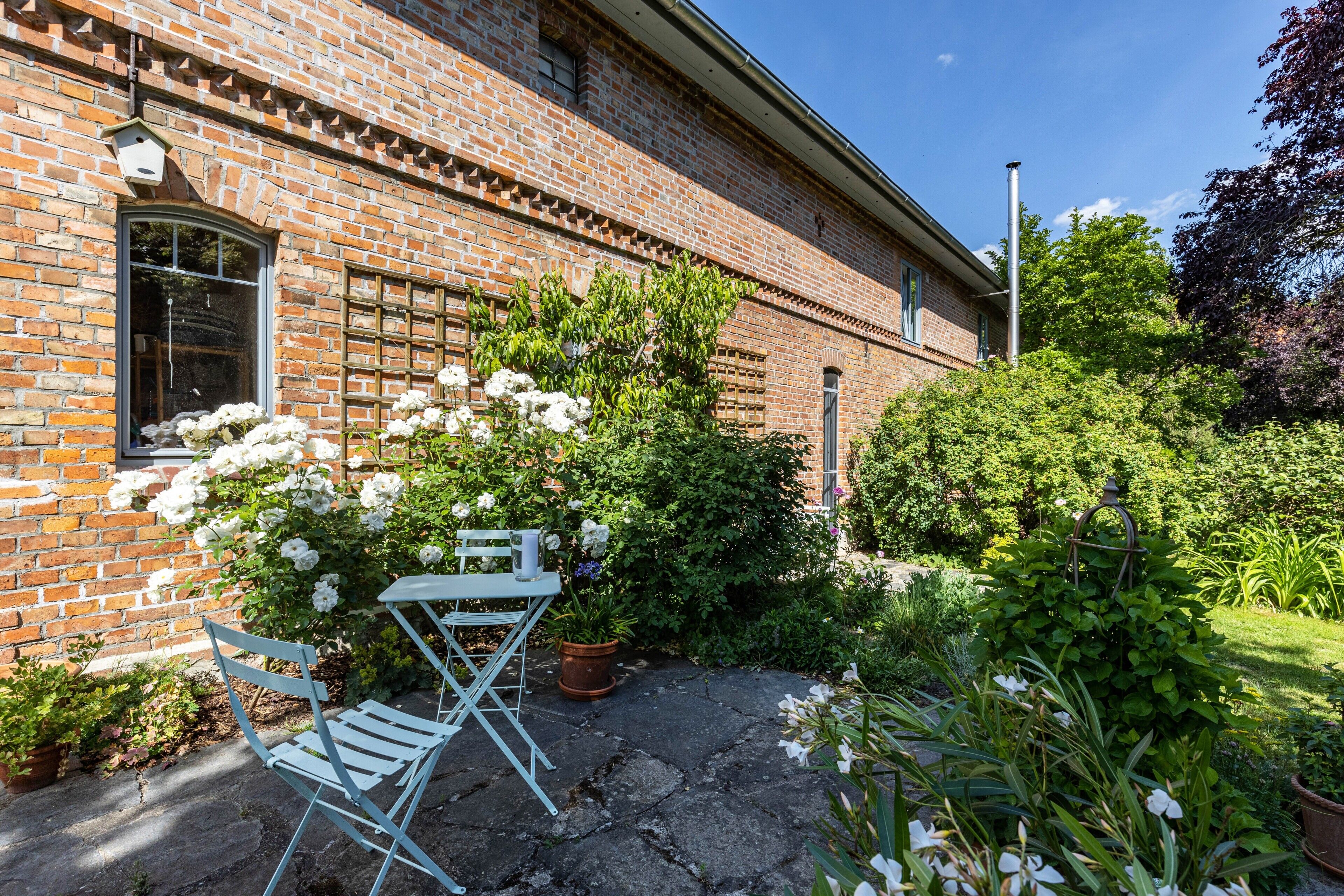 Un bâtiment en briques avec un jardin, une chaise pliante blanche et une plante en pot.