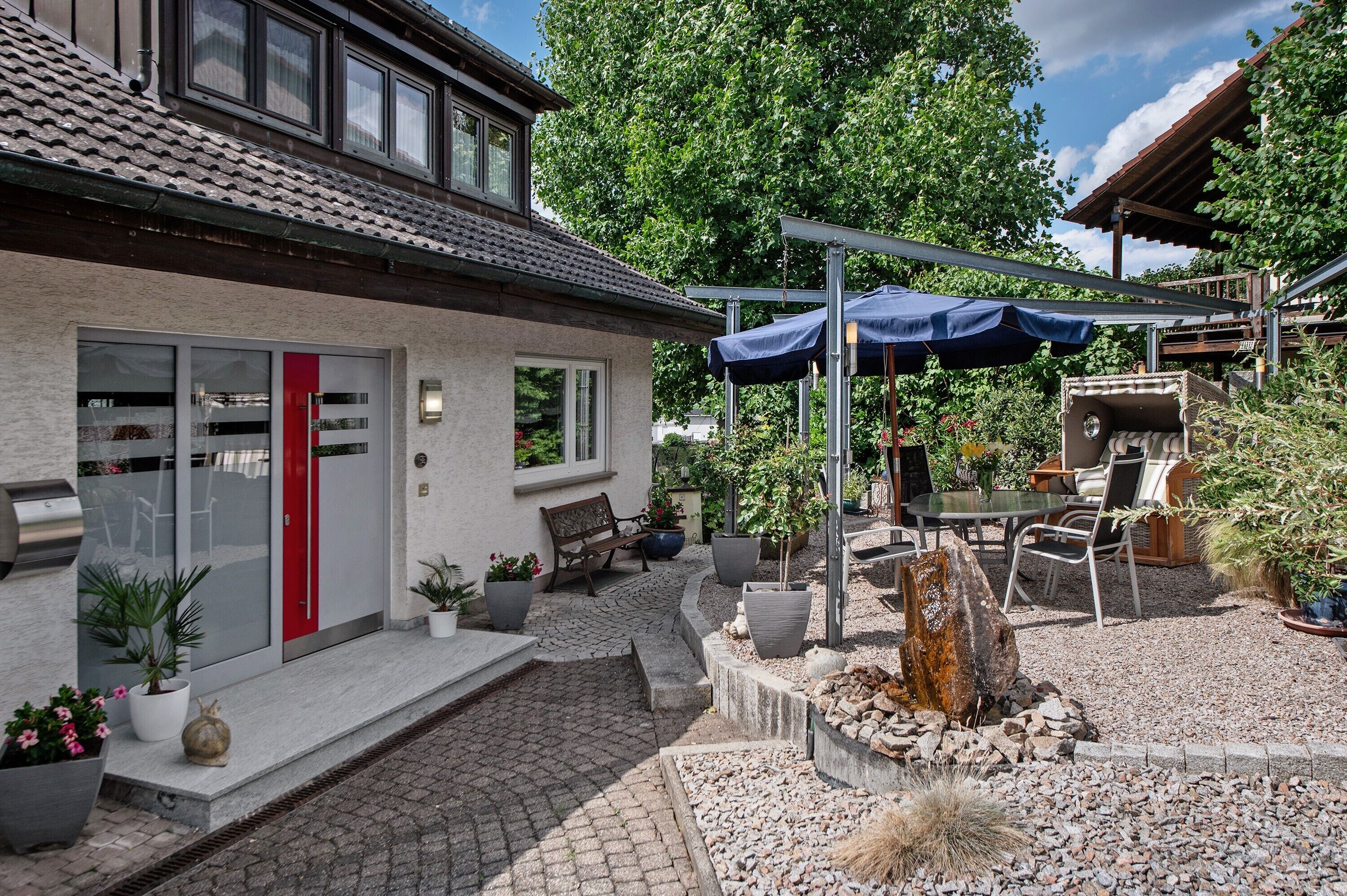 A house with a red door, a patio with outdoor furniture, and a pergola with a blue canopy.