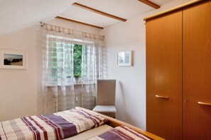 A bedroom with a bed, a chair, a wooden wardrobe, a window with sheer curtains, and two framed pictures on the wall. - Apartment 'Gerhard Lang' with Private Terrace, Shared Garden and Wi-Fi (Bad Bellingen)
