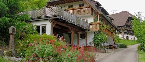 A traditional chalet with a wooden balcony, a stone pathway, and lush greenery.