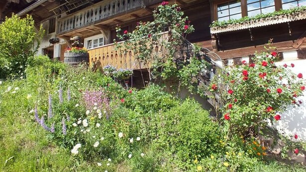 Un edificio de madera tradicional con balcones, rodeado de exuberante vegetación y diversas plantas florecientes.