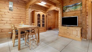 Un interior de madera con una mesa de comedor, sillas, un televisor en un mueble y un cuadro en la pared.
